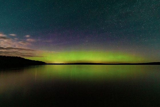 “Spring aurora borealis on Douglas Lake," University of Michigan Biological Station, Pellston, Michigan. The sky is green, purple, pink and orange over the lake with land visible on the far shore.